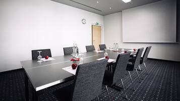 Un salón de conferencias con una larga mesa, sillas, una pantalla de proyector y un reloj en la pared.