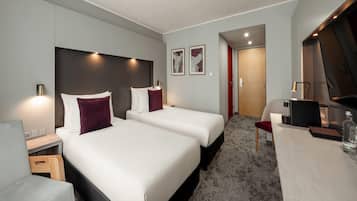 A hotel room with two beds, a desk, a chair, a TV, and a minibar.