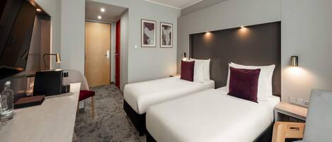 A hotel room with two beds, a desk, a chair, a TV, and a door leading to another room.