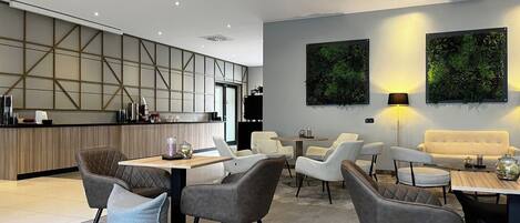 A modern hotel lobby with a central seating area, a kitchen, and two large wall-mounted plant displays.