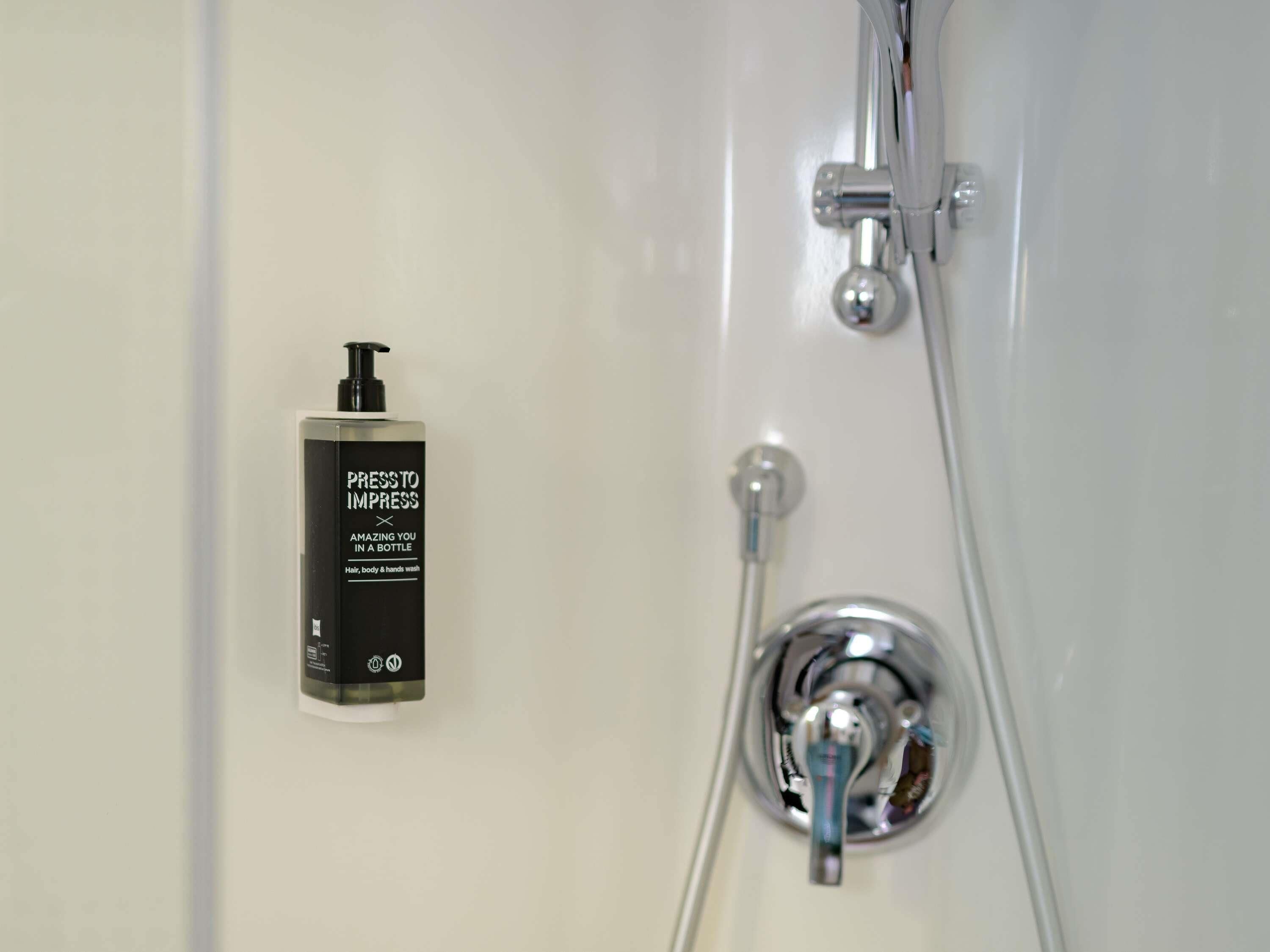A bathroom with a shower, a faucet, and a bottle of shampoo.