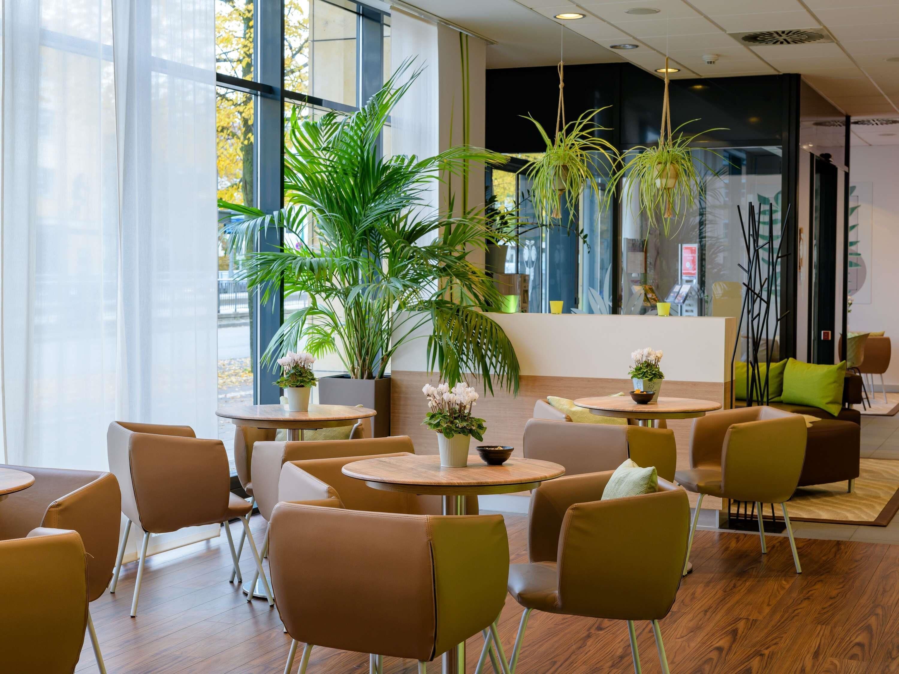 Een modern interieur met ronde tafels en stoelen, grote ramen en kamerplanten.