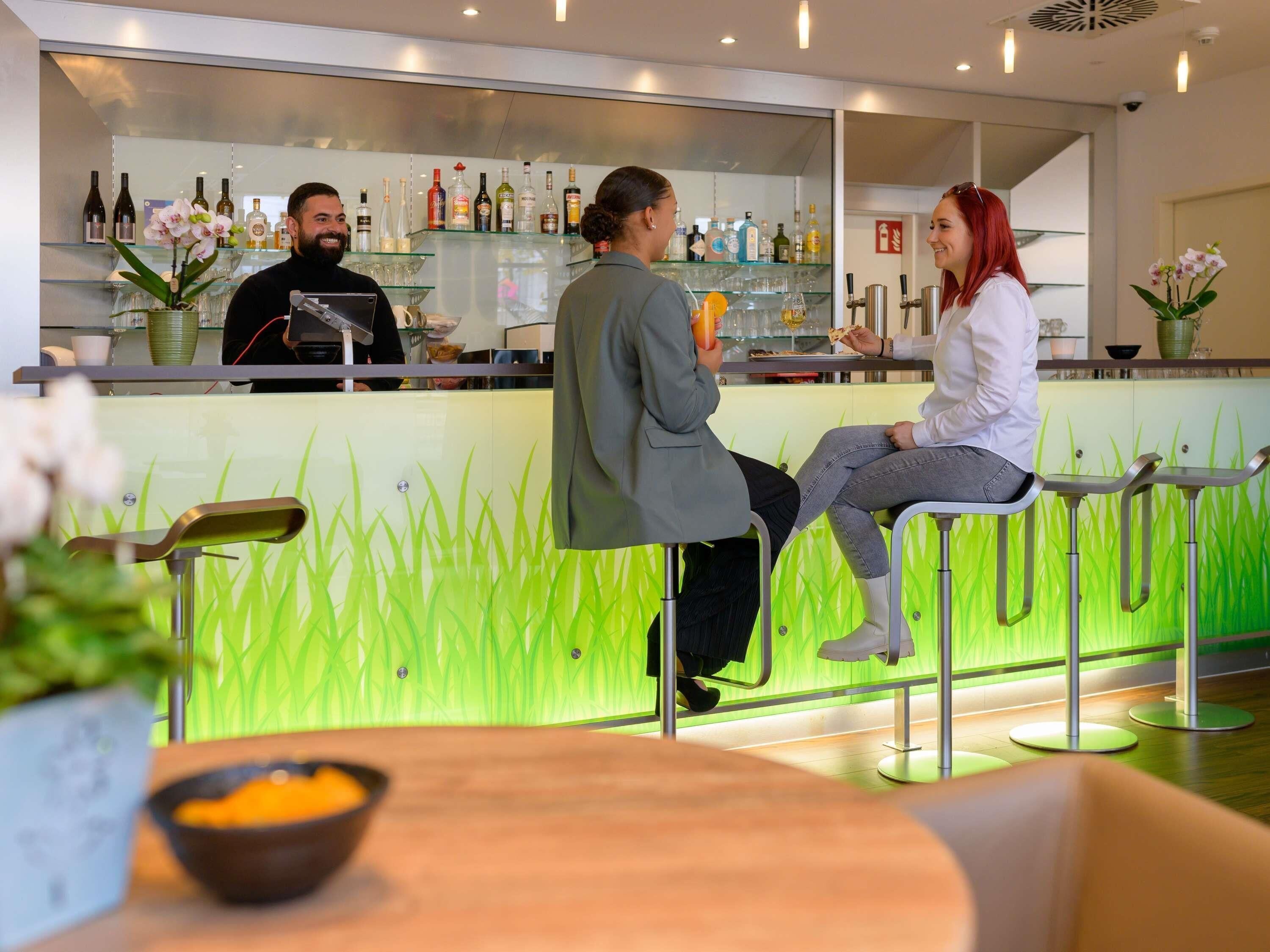 Eine Bar mit Theke, Barhocker und einer Sitzecke mit einer Wand, die wie grünes Gras wirkt.