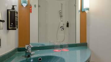 Un bagno con un lavandino verde, uno specchio, un soffione a mano e un dispenser per sapone.