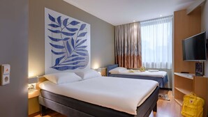 Habitación de hotel con una cama grande, una cama más pequeña, un televisor y un bolso amarillo en el suelo.