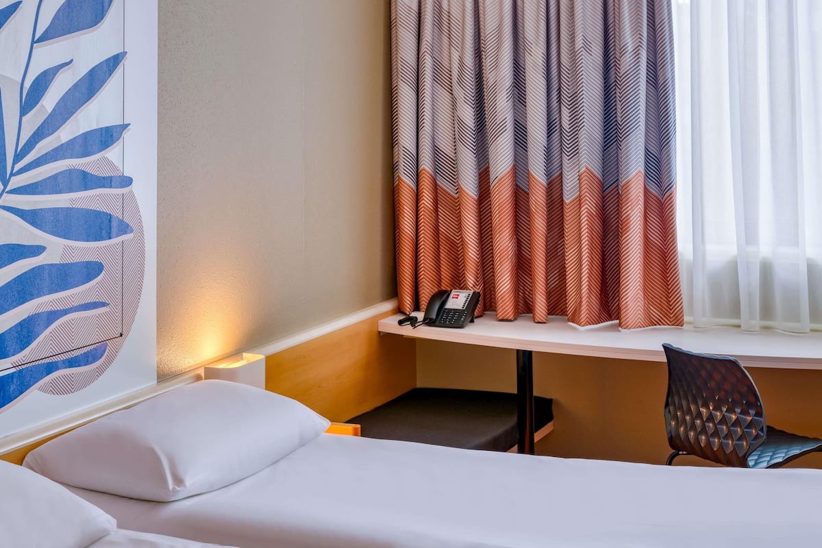 A hotel room with a bed, a desk with a telephone, and a chair.