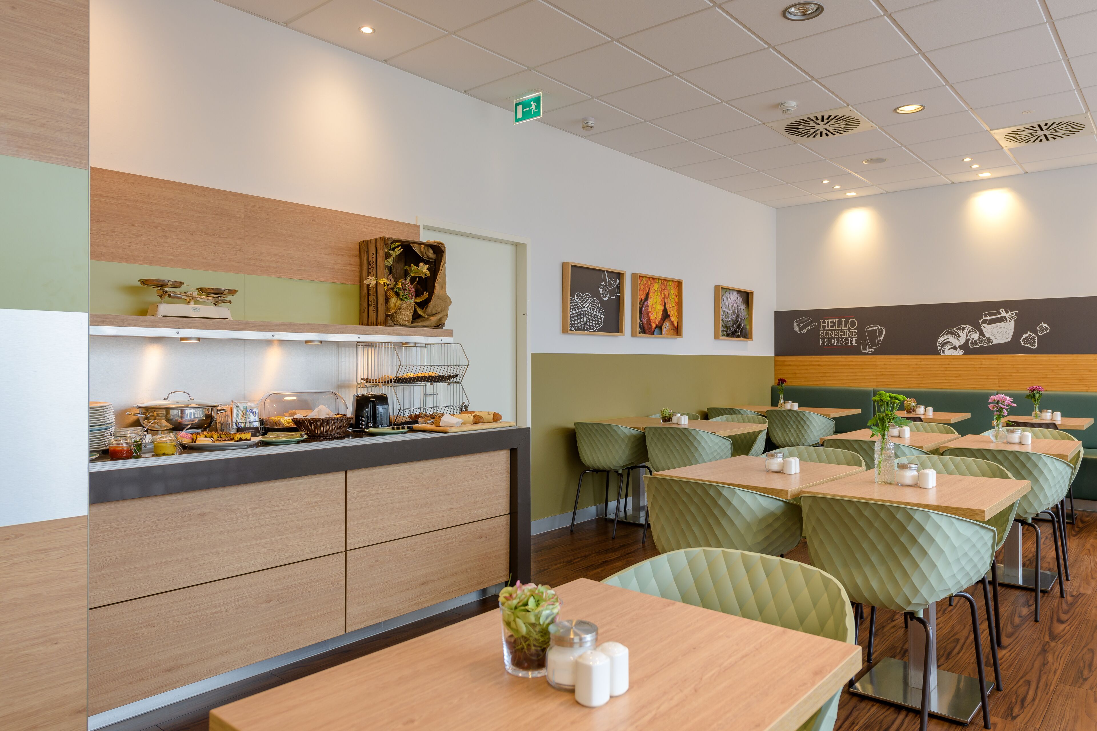A modern cafe with a buffet counter, green cushioned seating, and artwork on the walls.