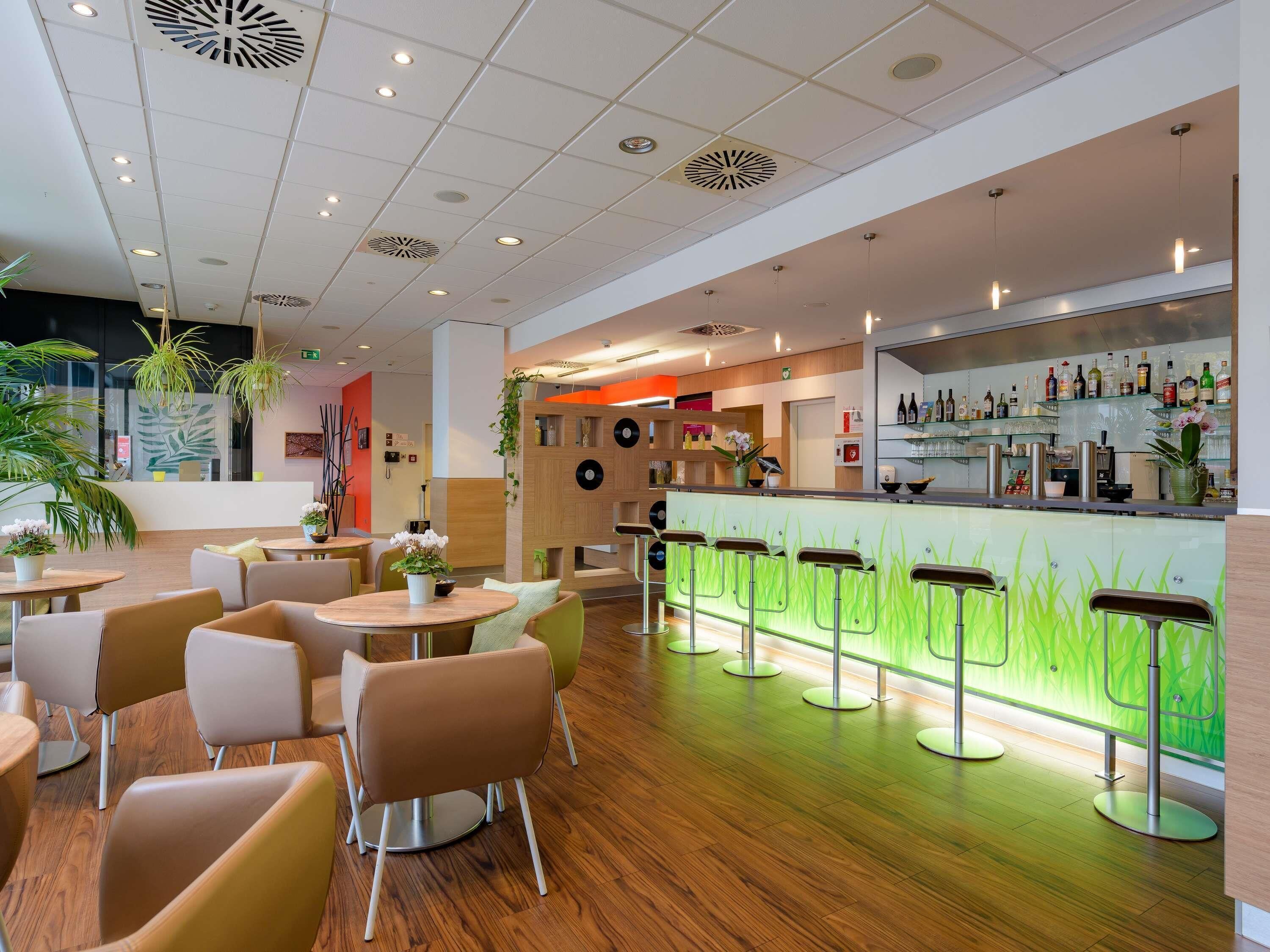 Uma área de bar moderna com balcão de neon verde, diversos arranjos de assento e piso de madeira.