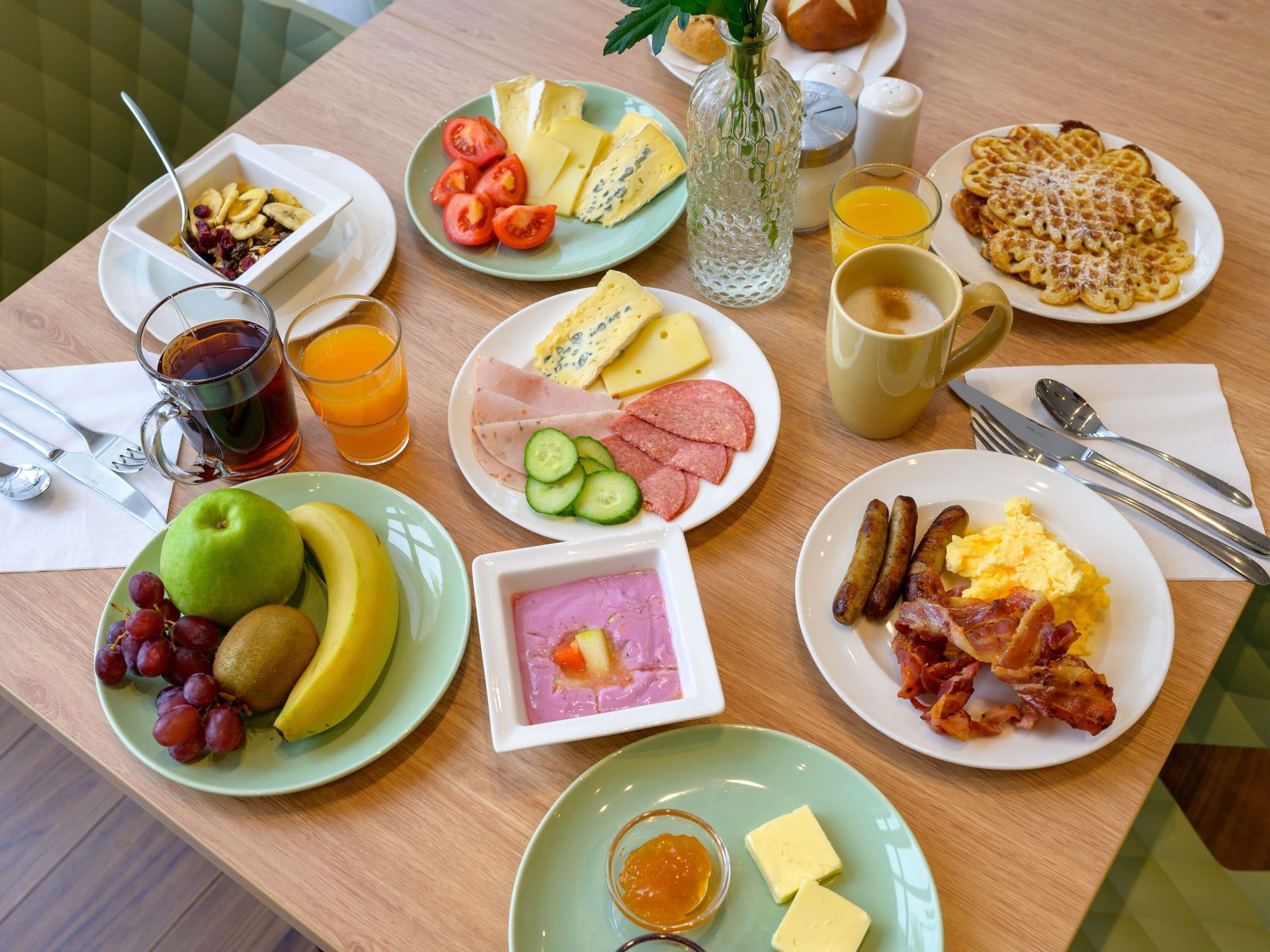 Una mesa de desayuno con diferentes alimentos, utensilios y un vaso de jugo de naranja.