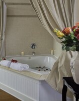 A bathtub with a towel and rose petals, a vase with flowers, and a curtain.