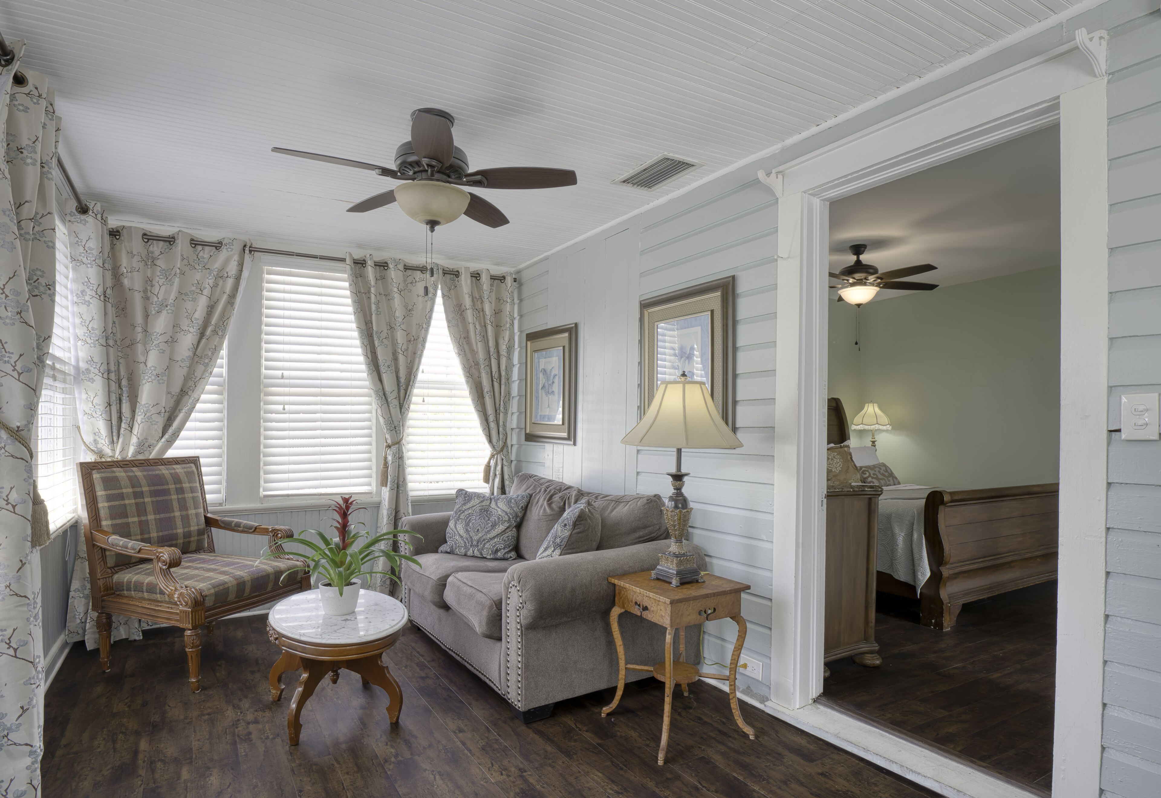A living room with a wooden floor, a sofa, a chair, a ceiling fan, and a lamp.