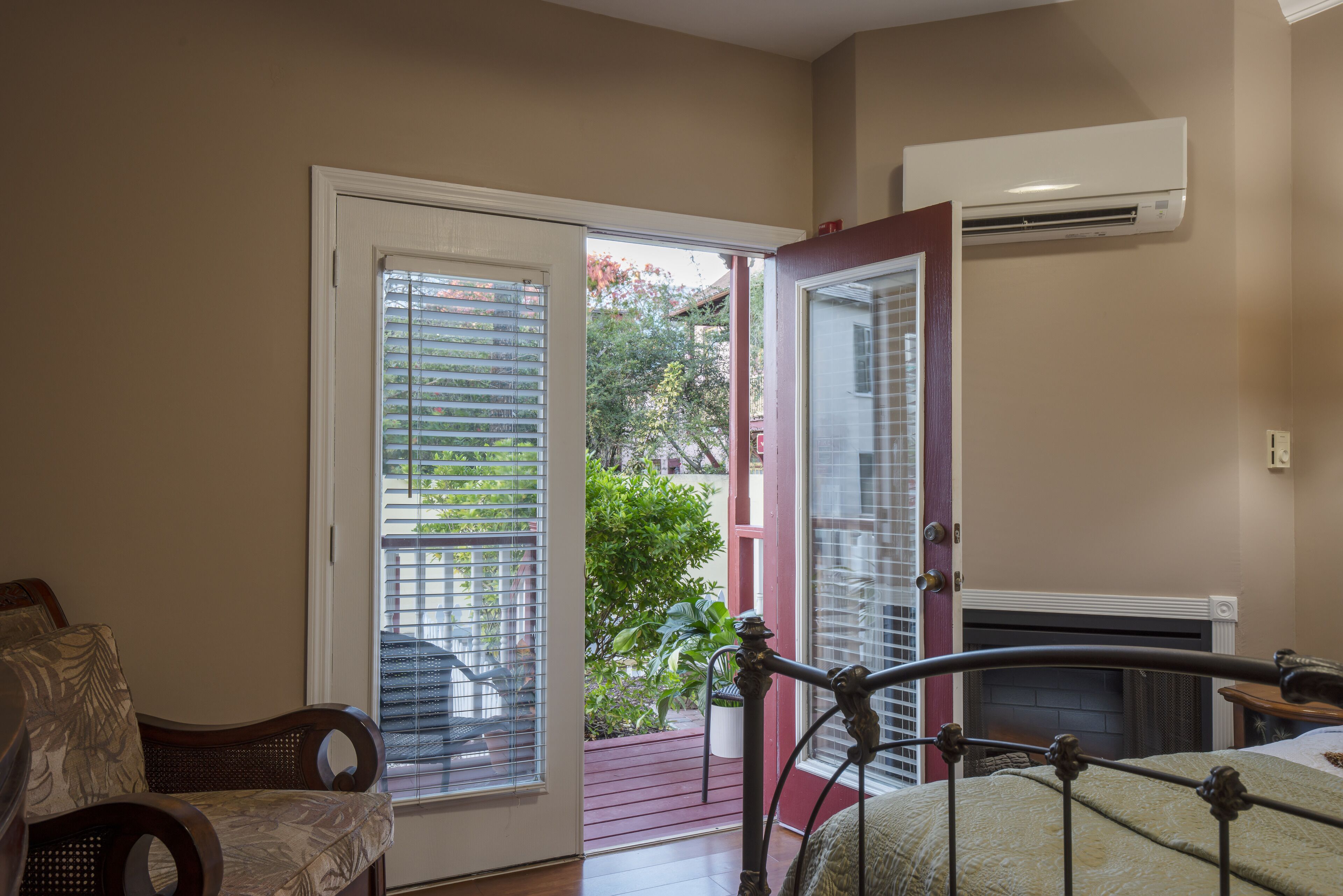 A bedroom with a bed, a chair, a door leading to a balcony, and an air conditioning unit.