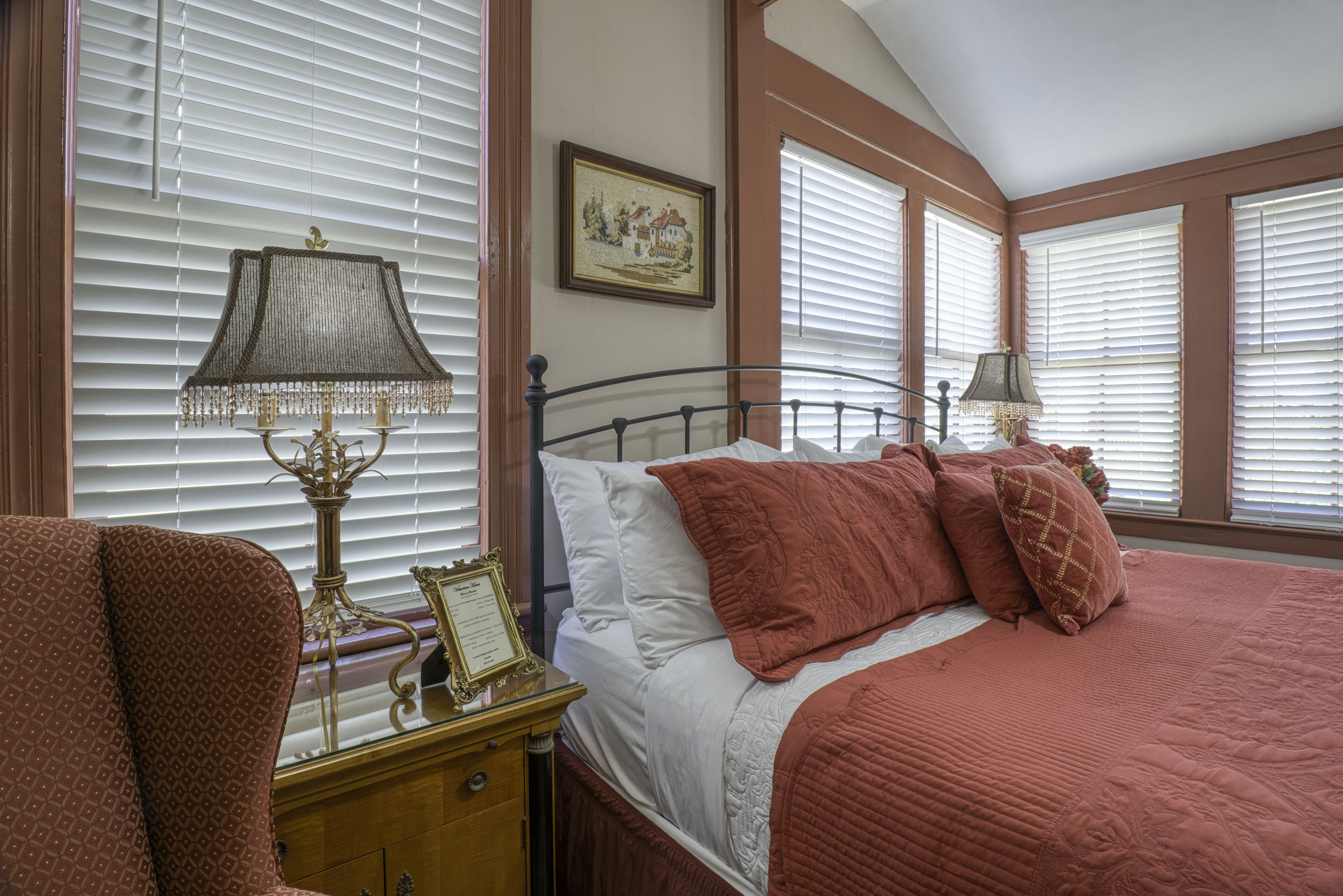 A bedroom with a bed, a nightstand, a lamp, and a window with blinds.