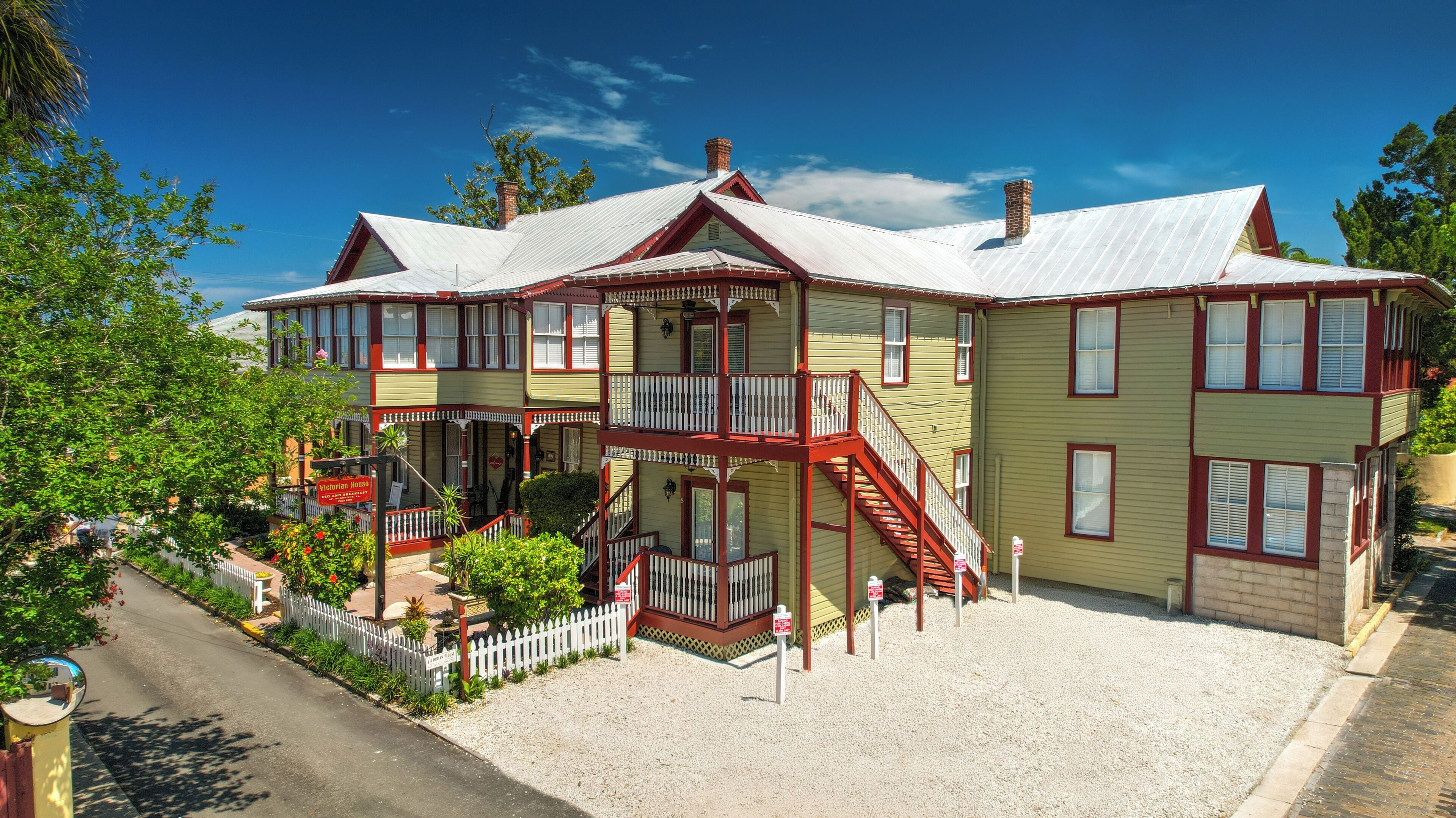 A Victorian-style house with a two-story balcony, a front porch, and a gravel driveway.