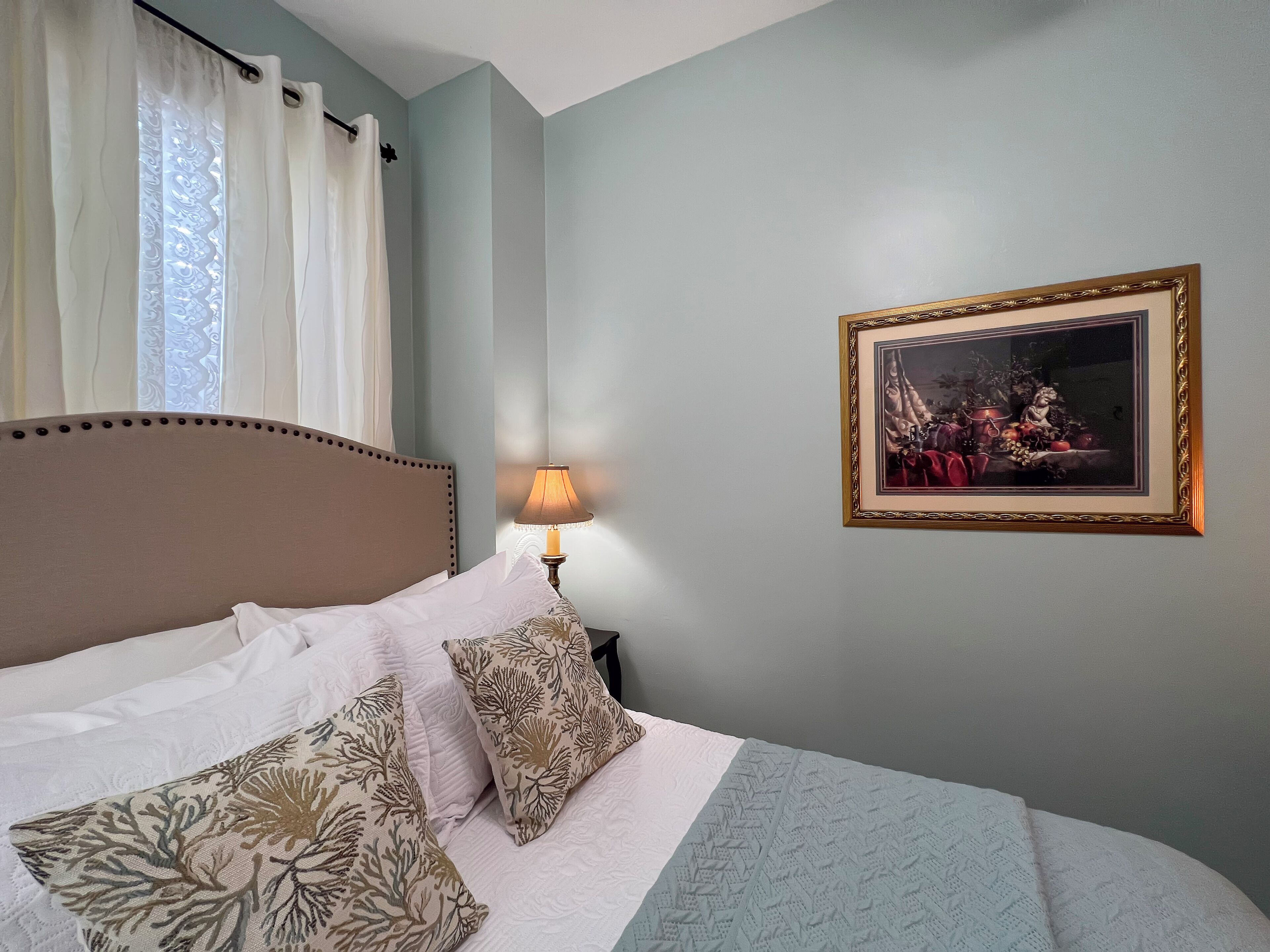 A neatly made bed with patterned pillows, a bedside lamp, and a framed artwork on the wall.