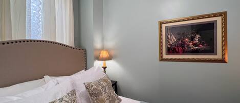 A neatly made bed with patterned pillows, a bedside lamp, and a framed artwork on the wall.