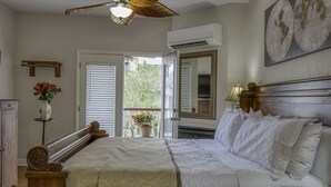 A bedroom with a large bed, a ceiling fan, an air conditioning unit, a world map on the wall, and a view of the outdoors through a door. - Victorian House Bed & Breakfast (St. Augustine)