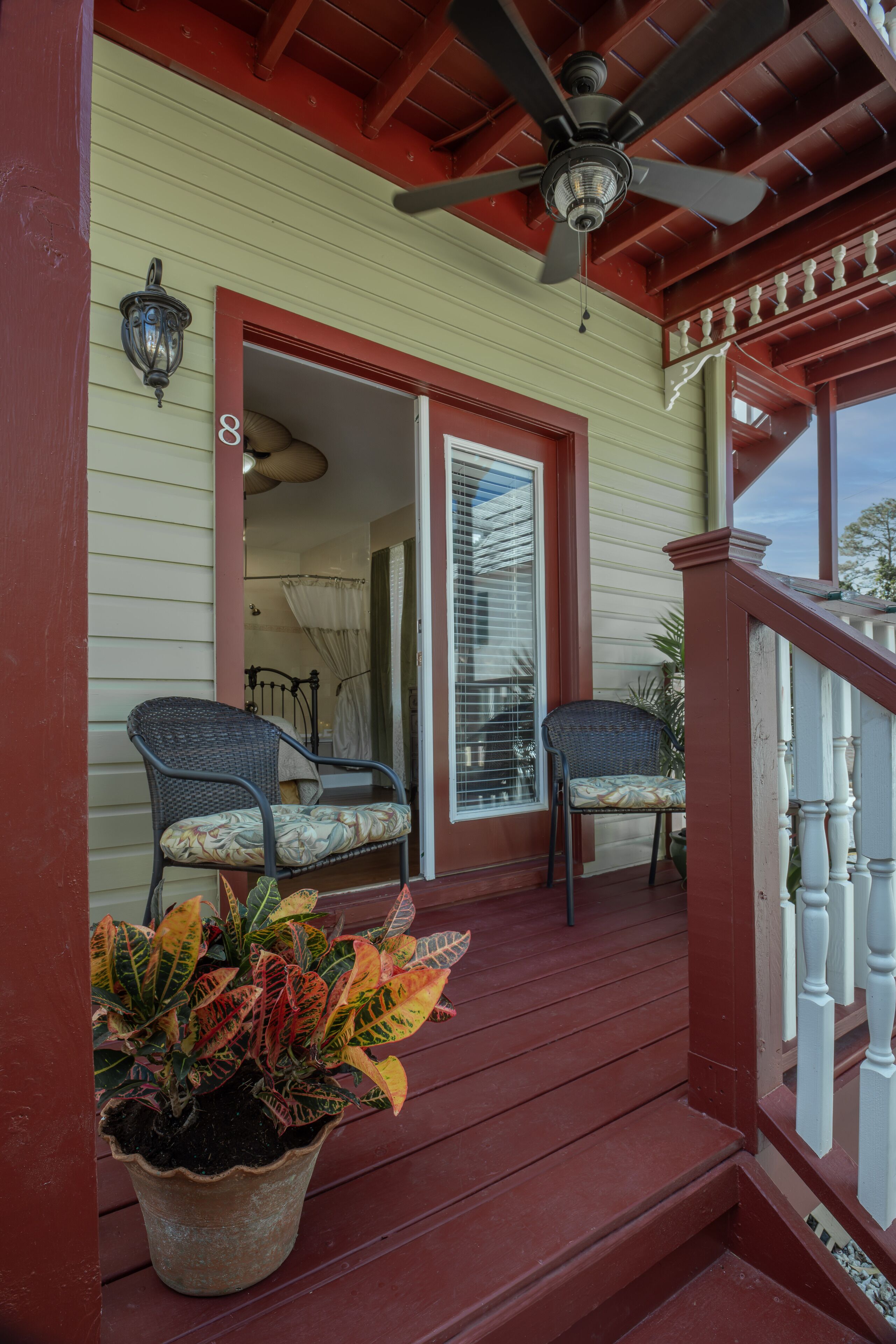 A porch with two wicker chairs, a potted plant, and a ceiling fan.