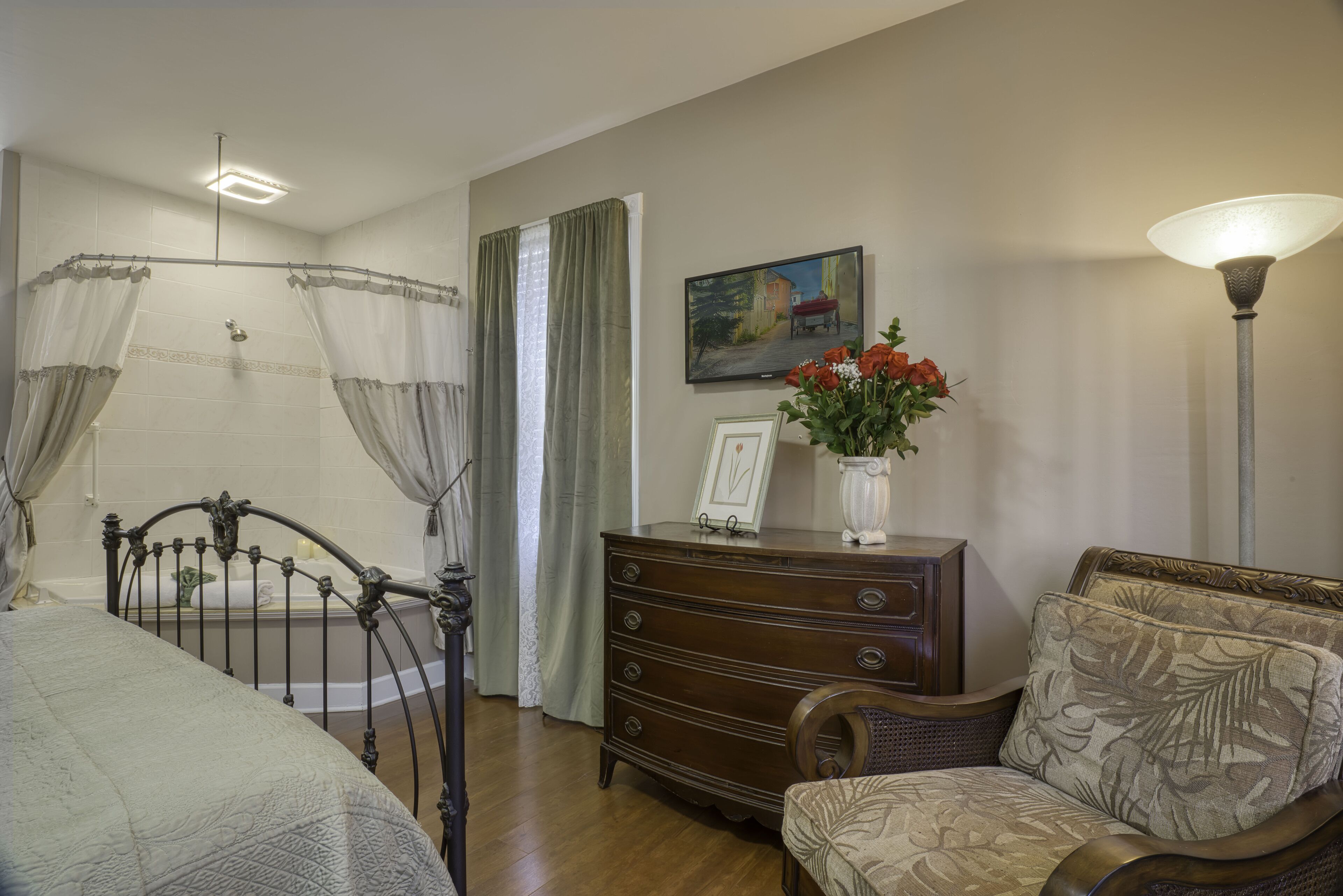 A bedroom with a bed, a wooden dresser, a chair, a painting, and a lamp.