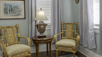 A room with a ceiling fan, two wicker chairs, a patterned rug, and a table with a lamp.