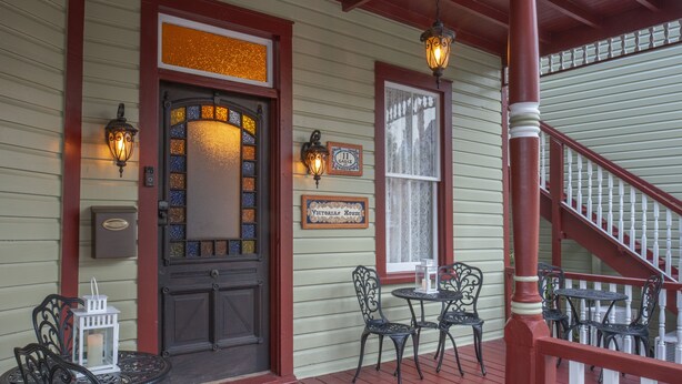 A porch with a wooden staircase, a door with a stained glass window, and two tables with chairs. - Victorian House Bed & Breakfast (St. Augustine)