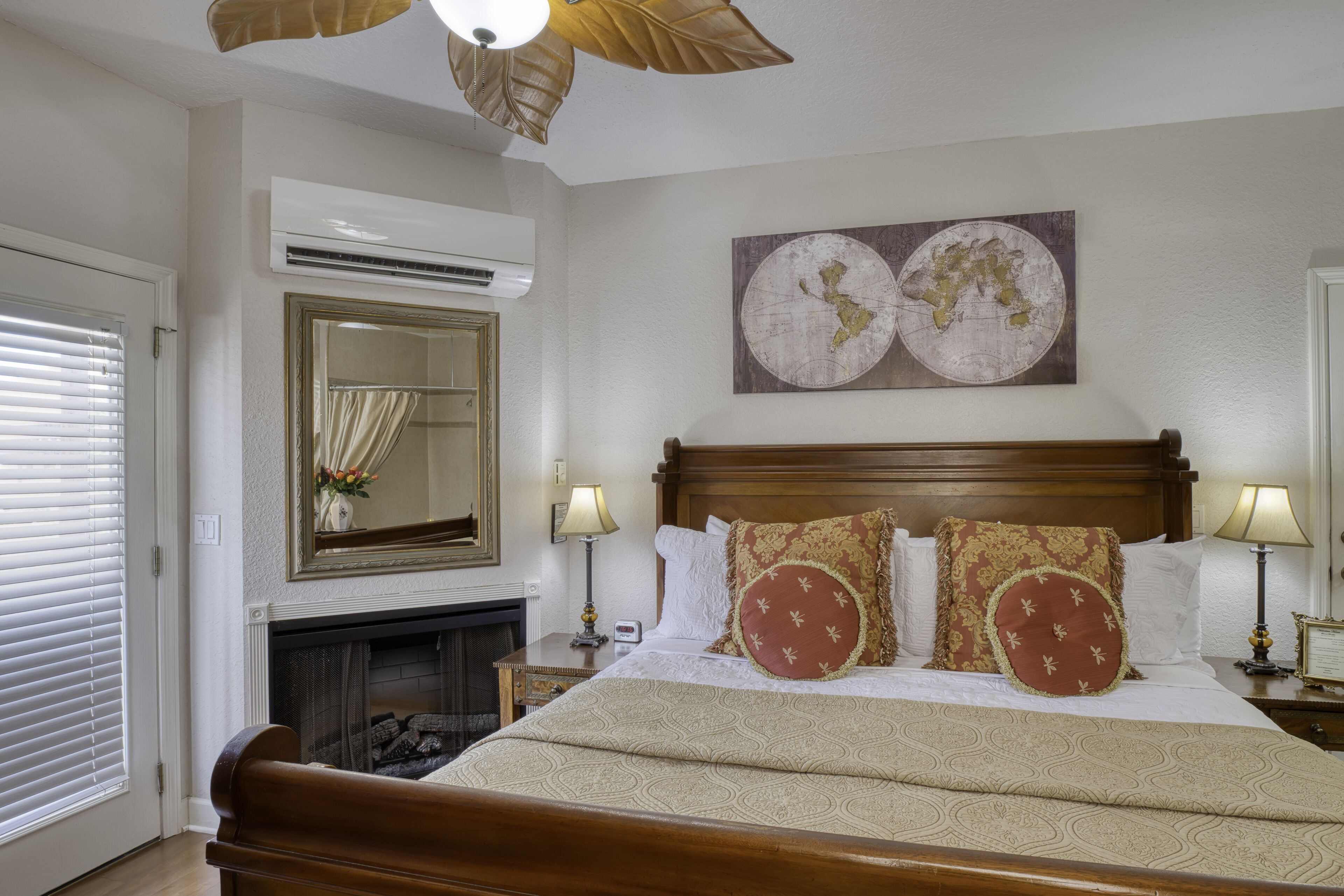 A hotel room with a large bed, a fireplace, a world map artwork, and a ceiling fan.
