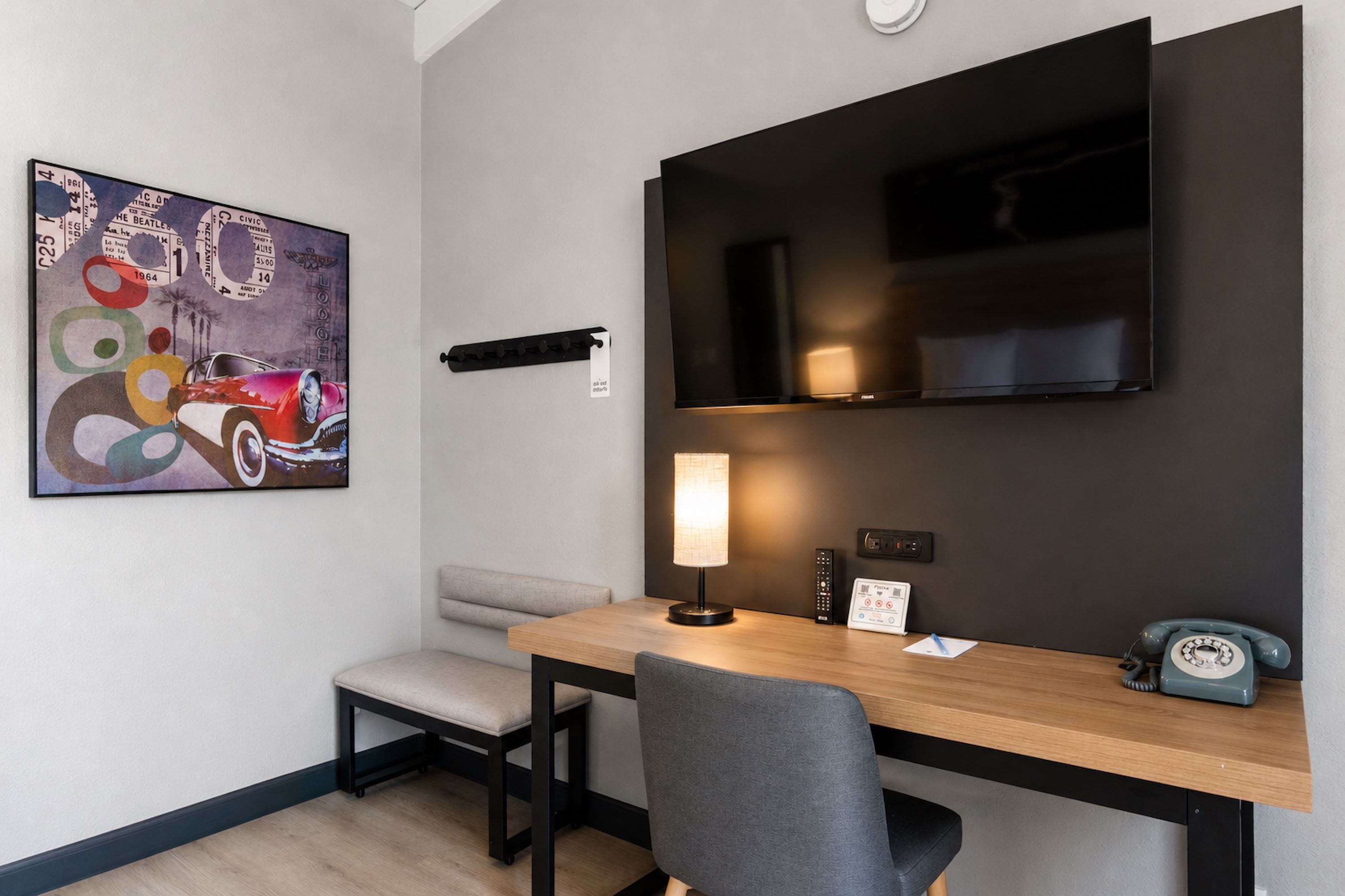 Une chambre d’hôtel moderne avec un bureau en bois, un téléviseur fixé au mur, un tableau, une lampe et un téléphone.