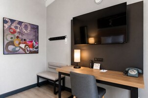Una habitación de hotel moderna con un escritorio de madera, un televisor montado en la pared, un cuadro, una lámpara y un teléfono.