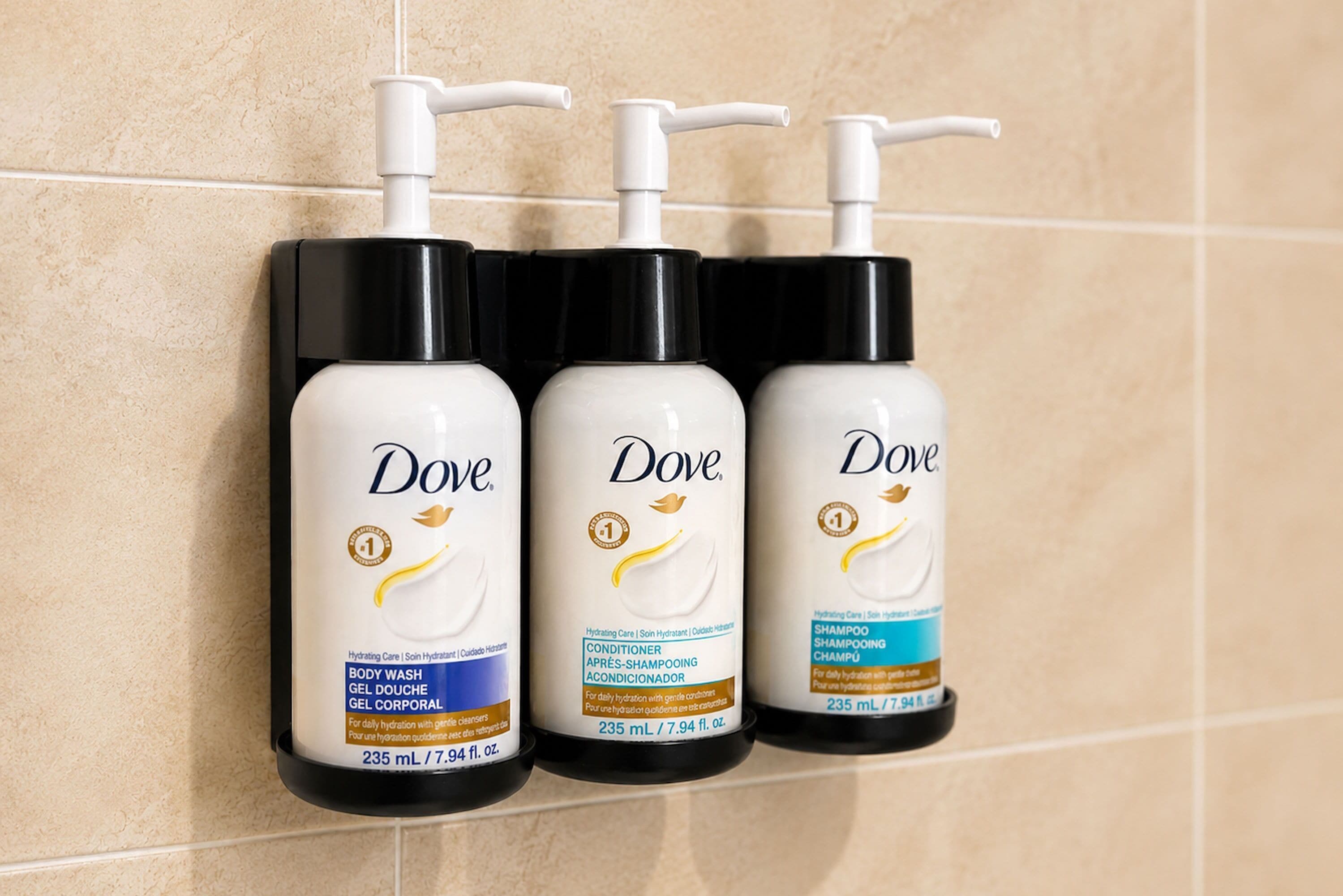 Three Dove body wash bottles on a tiled wall.