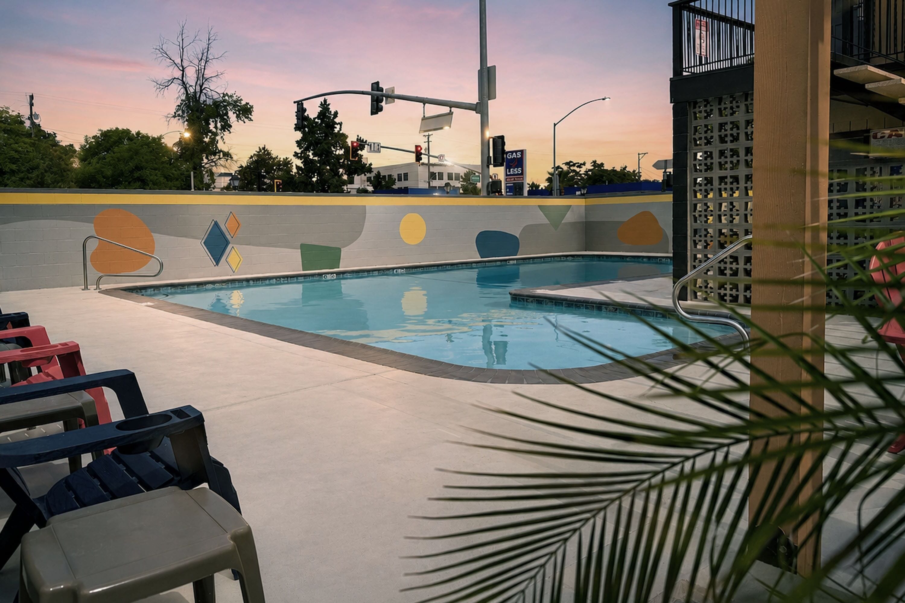 Una piscina con sillas de descanso, un edificio con arte mural geométrico y una calle con semáforos.