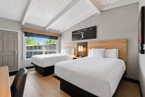 A hotel room with two beds, a desk, and a window with a view of a building. - Thunderbird Lodge (Redding)