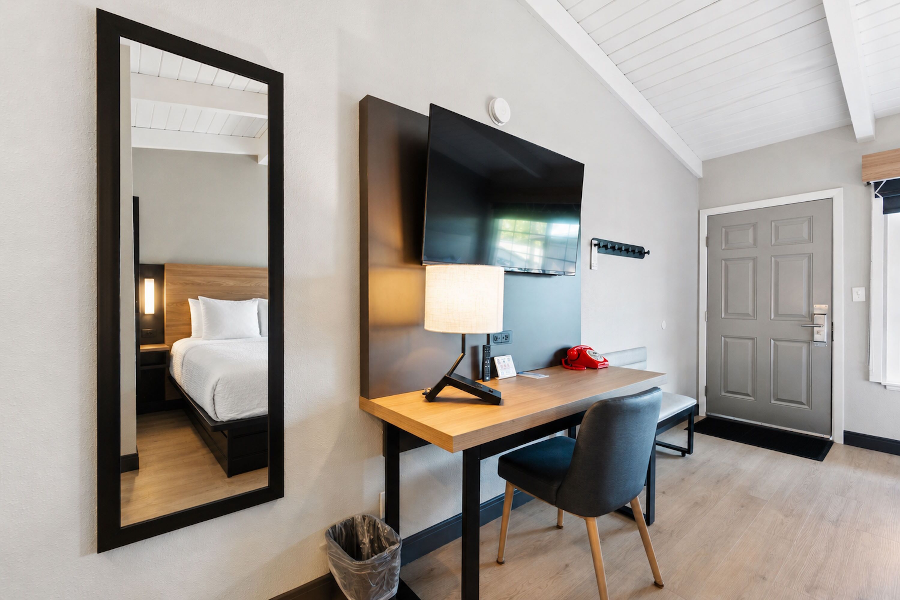 Een hotelkamer met een bed, bureau, stoel, televisie en een deur.