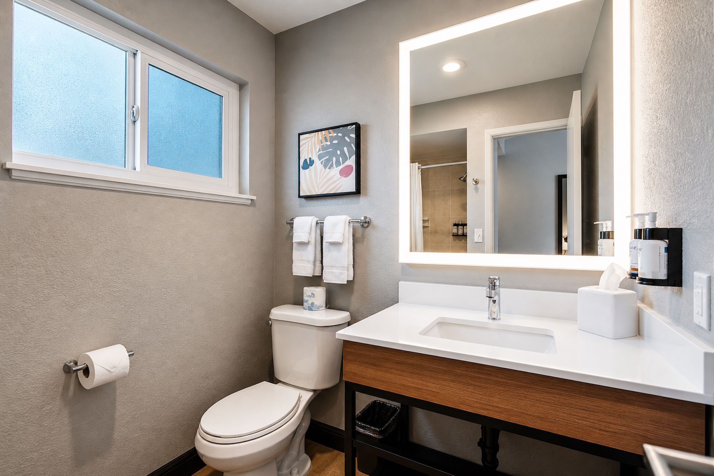 A bathroom with a toilet, sink, mirror, and window.