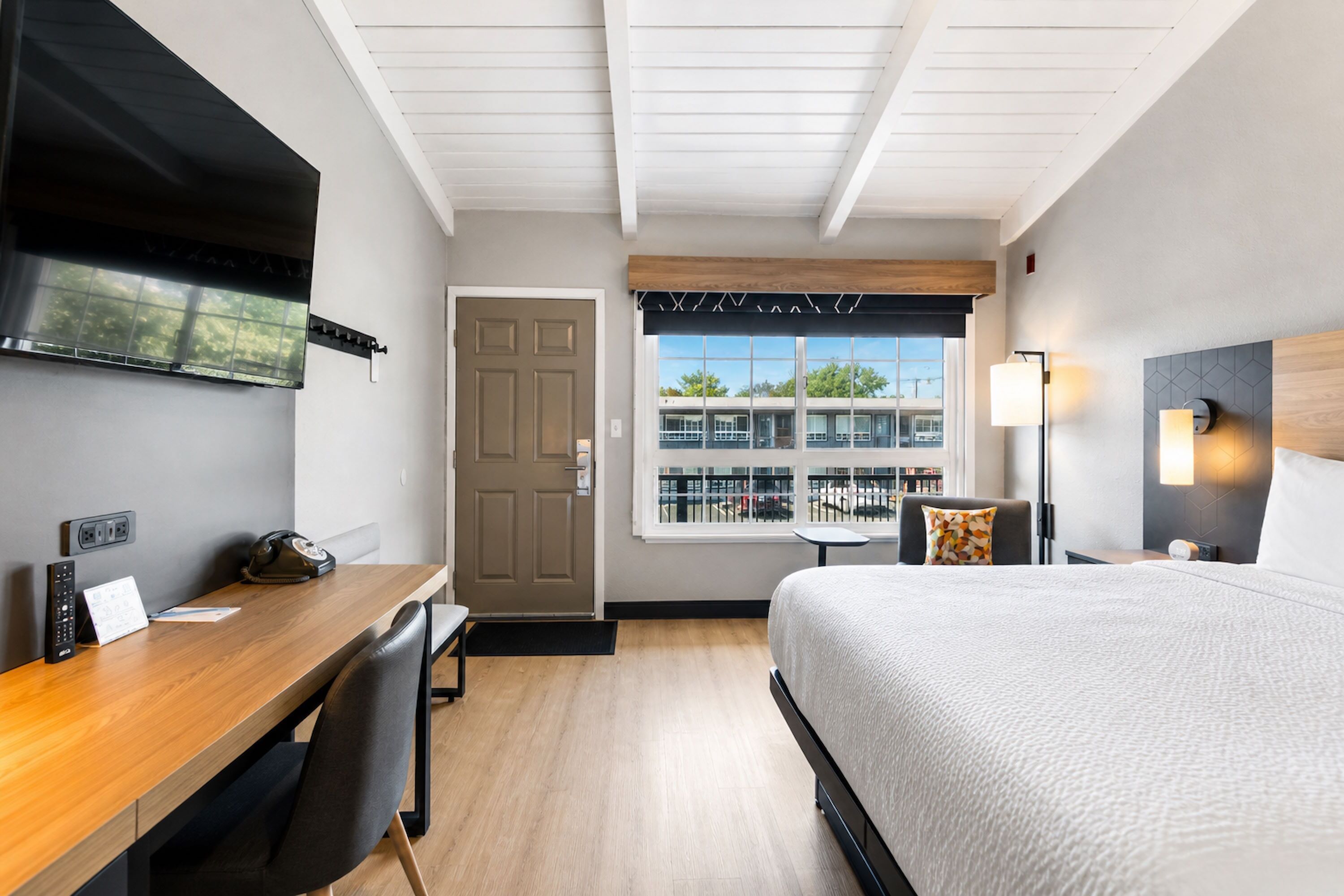 Ein Hotelzimmer mit Bett, Schreibtisch, Stuhl, Fernseher, Fenster und Lampe.