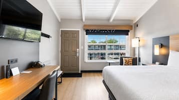 A hotel room with a bed, desk, chair, TV, window, and lamp.