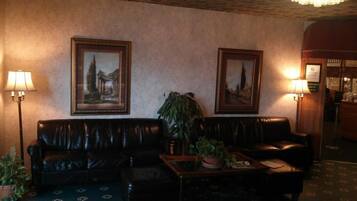 A hotel lobby with leather sofas, a coffee table, two framed paintings, and a chandelier.