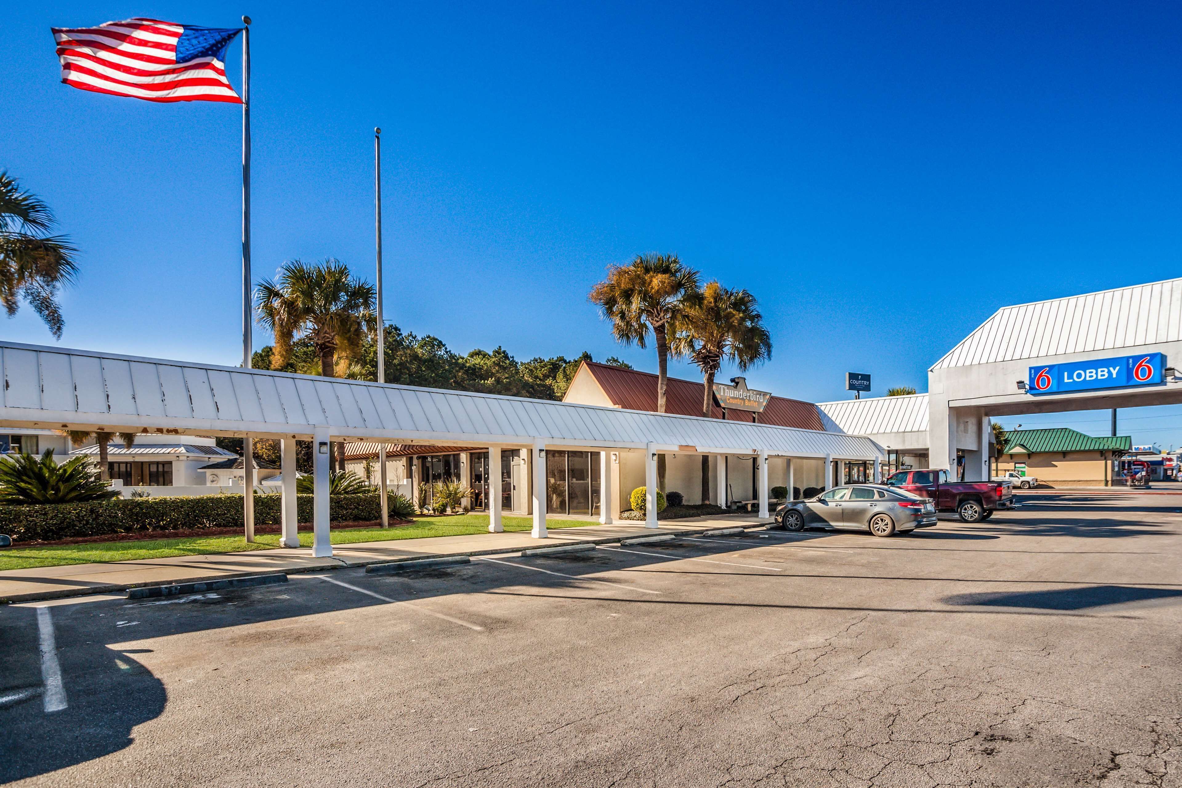 A hotel with a covered outdoor area, a flagpole with an American flag, and a sign indicating a lobby.