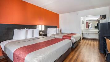 A hotel room with two beds, a wooden floor, and an orange accent wall.