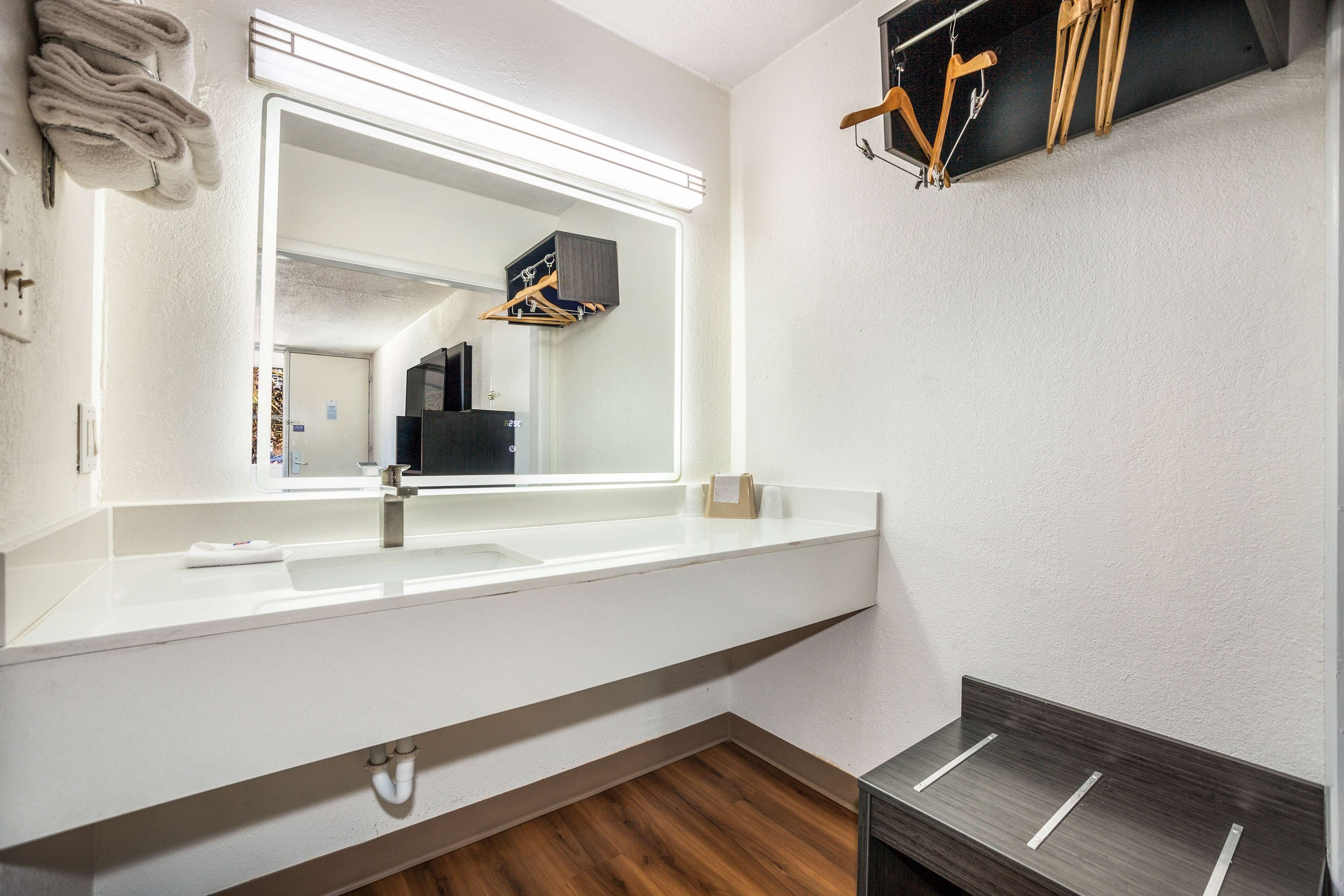 A modern bathroom with a large mirror, white countertop, and wooden flooring.