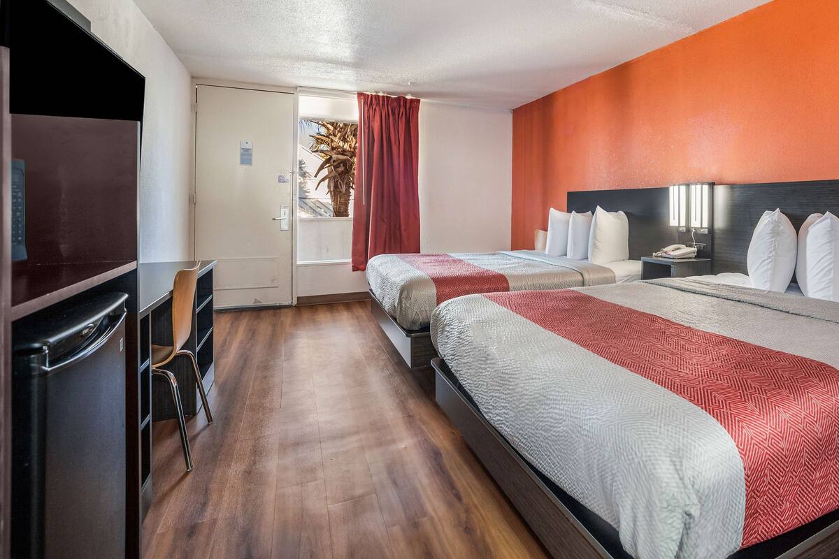 A hotel room with two beds, a desk, a chair, and a refrigerator.