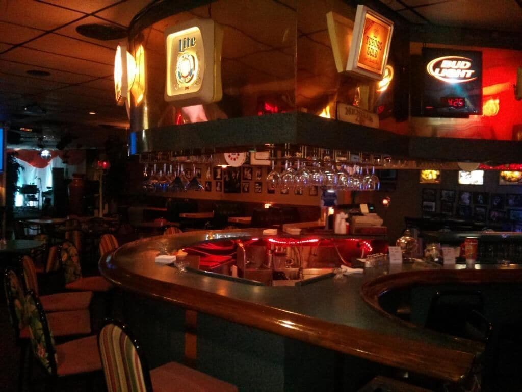 A bar area with a counter, bar stools, and a variety of bottles and glasses.