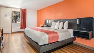 A modern hotel room with a large bed, a nightstand, a desk, and a window with curtains.
