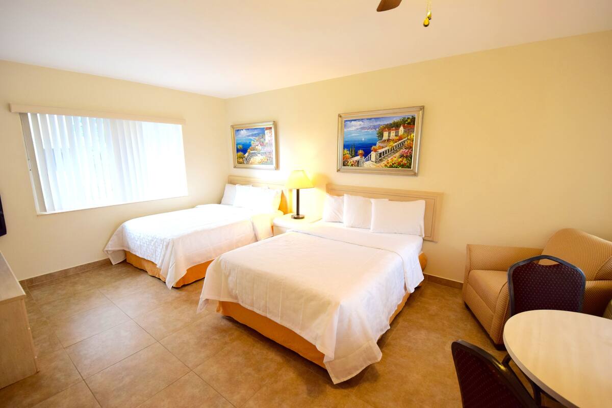 A hotel room with two beds, a sofa, a dining table, and two paintings on the wall.