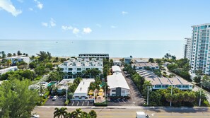 A coastal hotel with multiple buildings, a parking lot, and a view of the ocean.