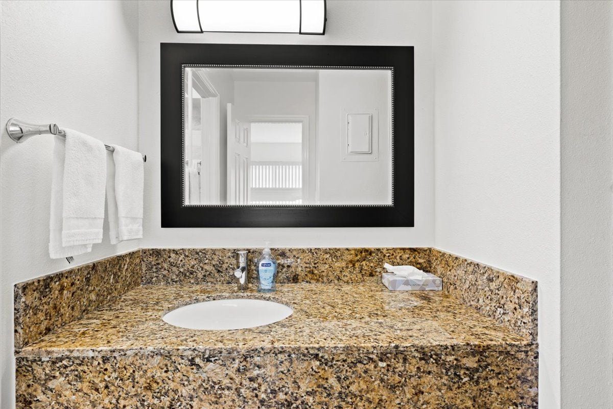 A bathroom with a granite countertop, a white sink, a mirror with a black frame, and two white towels hanging on a towel rack.