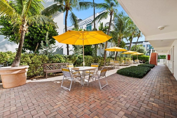 An outdoor patio with brick flooring, yellow umbrellas, and a seating area with chairs and a table.