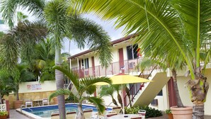 A poolside area with lounge chairs, a yellow umbrella, and a staircase leading to a balcony.