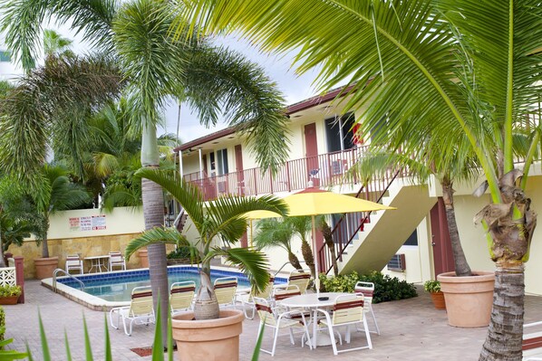Zona de piscina con sillones de descanso, una sombrilla amarilla y una escalera que conduce a un balcón.