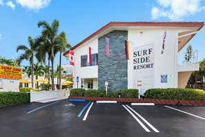 Edifício do SURF SIDE RESORT com fachada de pedra, várias bandeiras e estacionamento com vagas demarcadas.