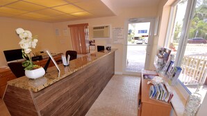 A reception desk with a wooden counter, a potted orchid, and a bulletin board with house rules.